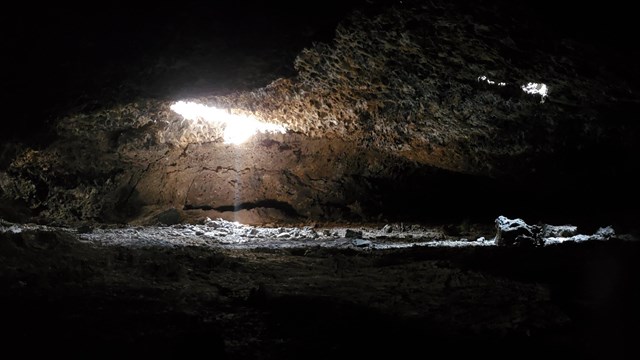 light illuminating part of a wide cave passage from the ceiling which is covered with small lava sta