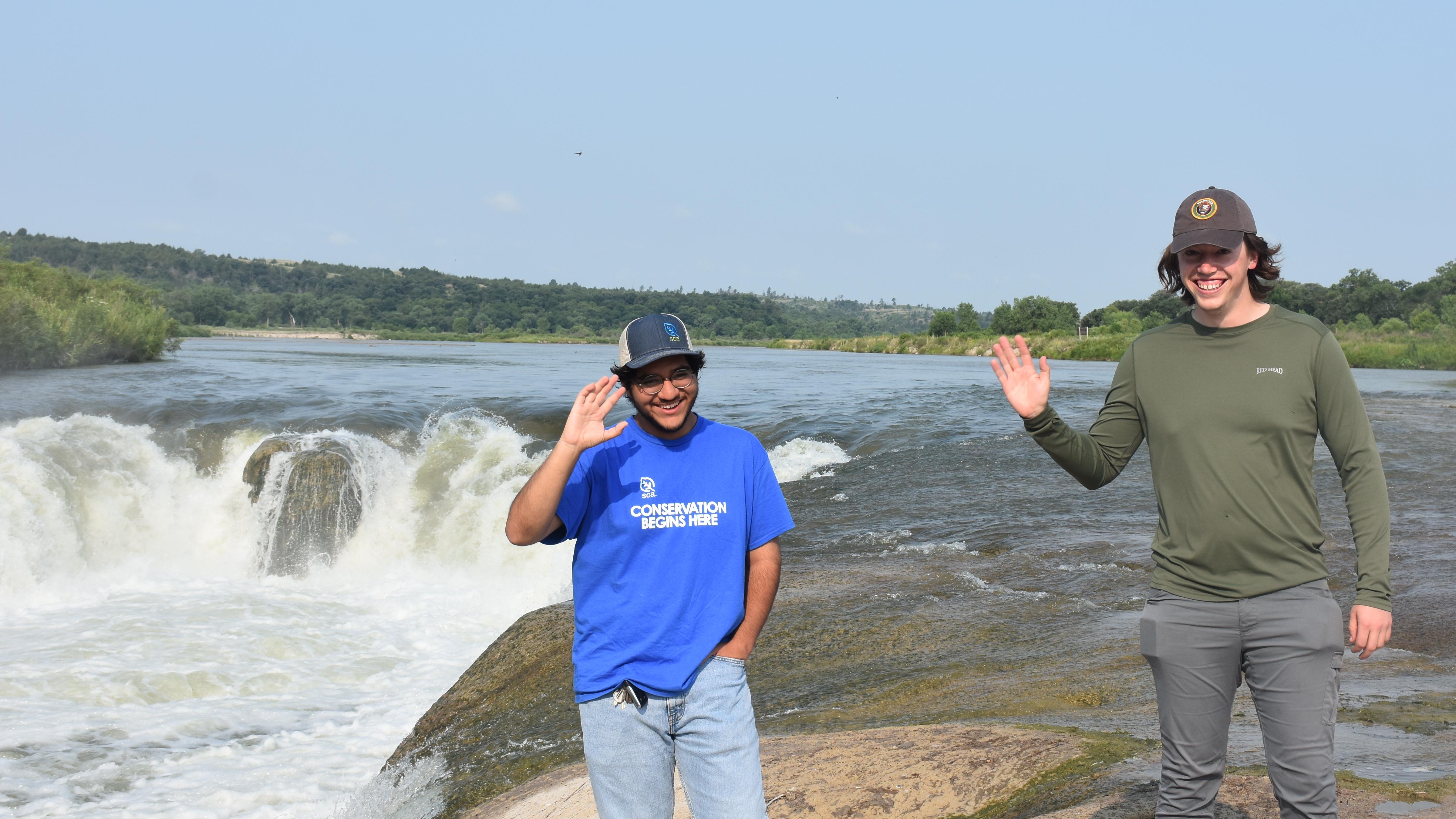 An Intern and a volunteer stand in front of rapid with high drop. 