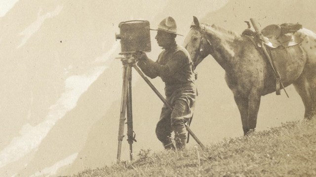 a historic photo of a man taking a photo with a horse behind him