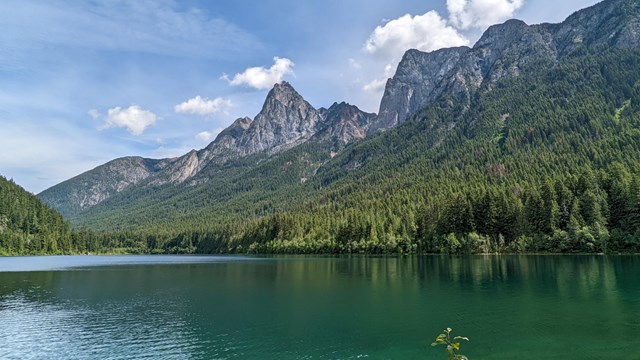 a green lake with clouds and mountains in the background