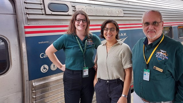 Trails & Rails volunteers stand posing and smiling in outside next to an Amtrak train 