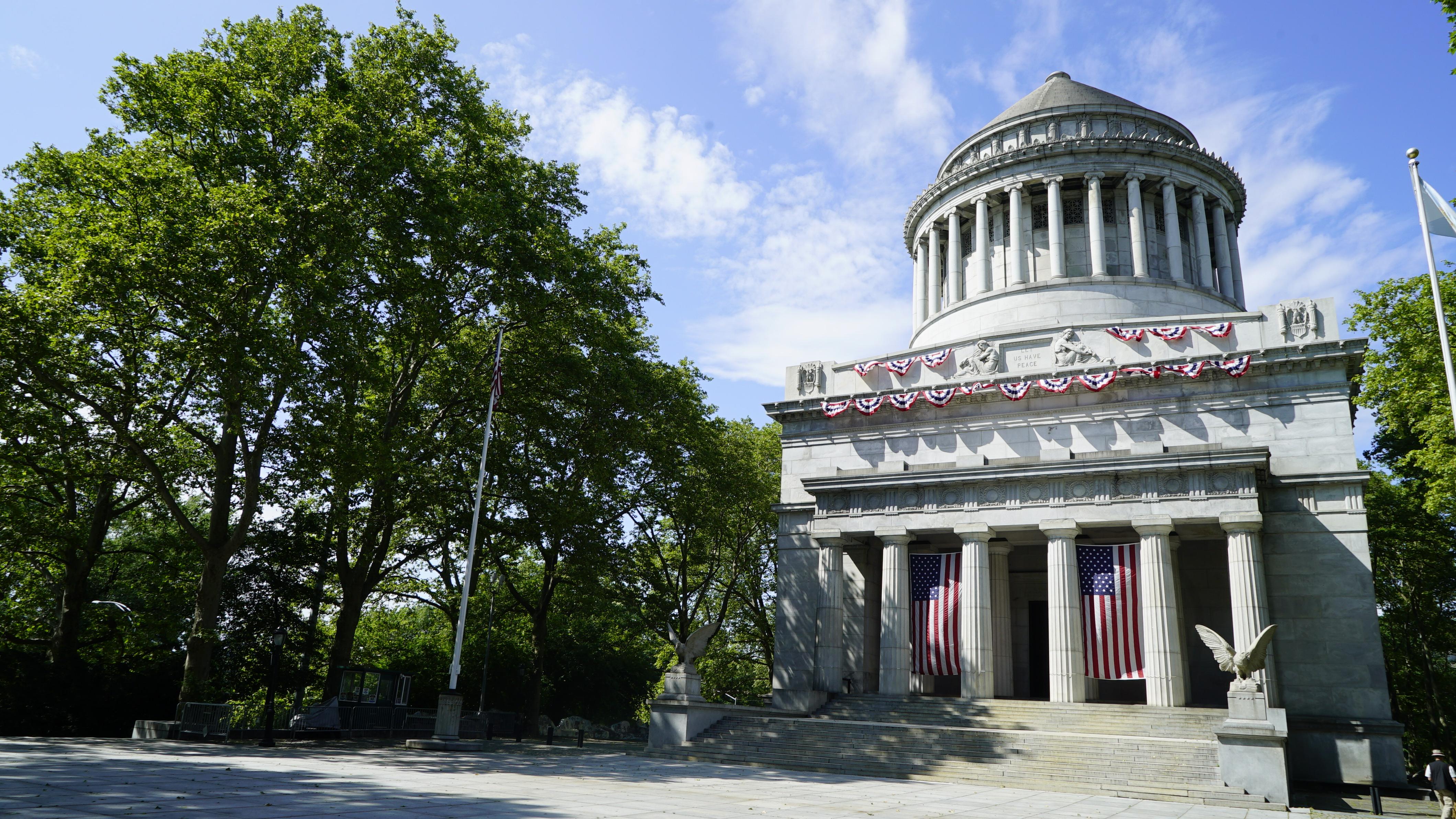 A marble mausoleum with a large dome stands tall against a bright blue sky 