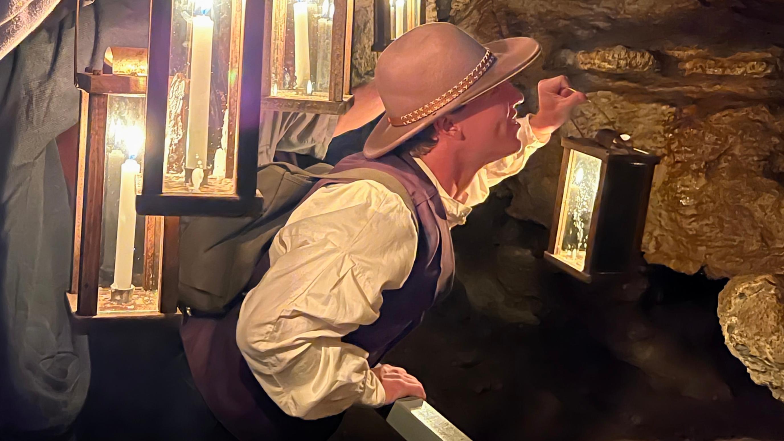 Rangers in pioneer clothing holding glass candle lanterns admiring the cave.