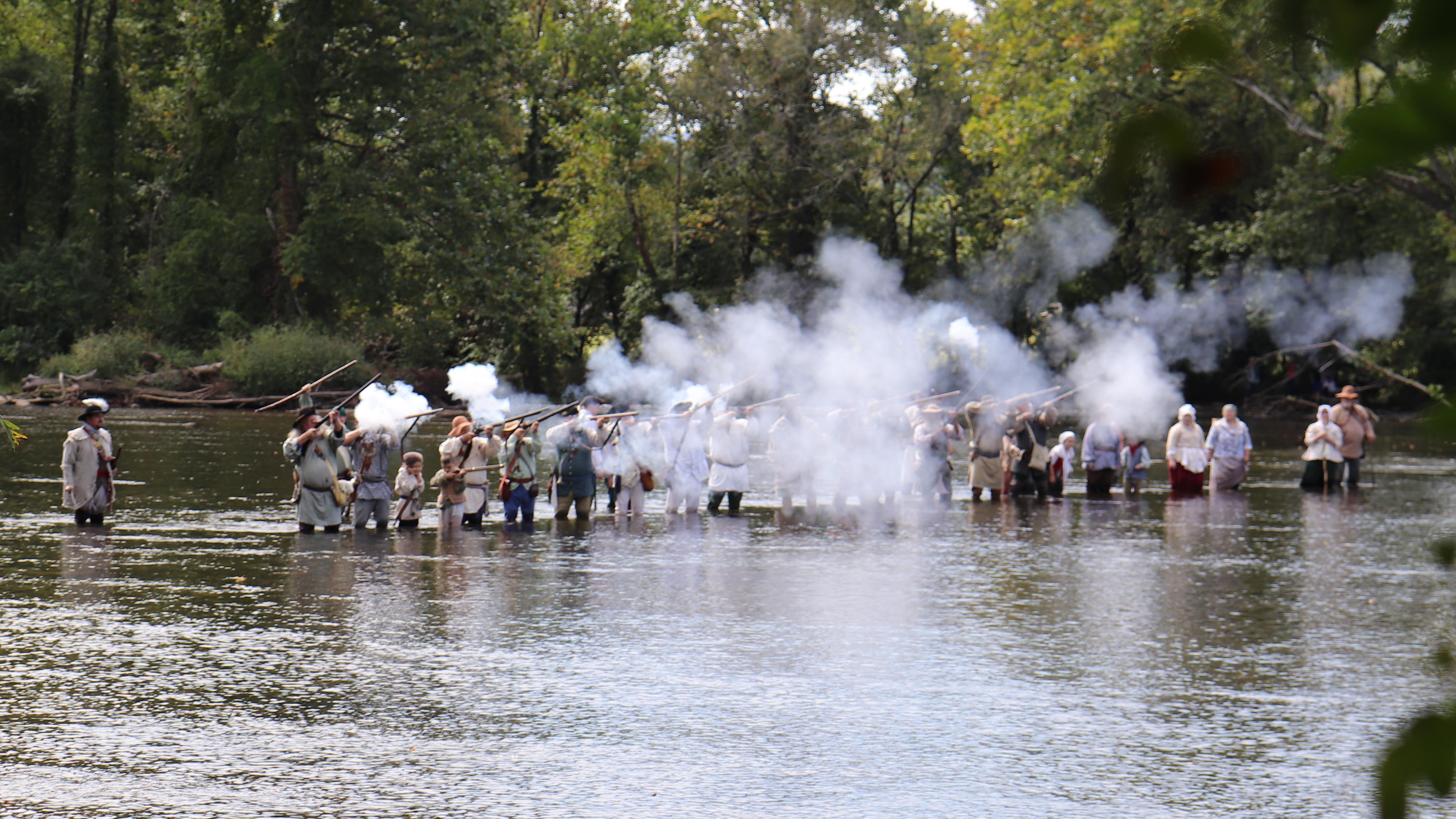 A group in costume fire historic weapons while standing in a river.