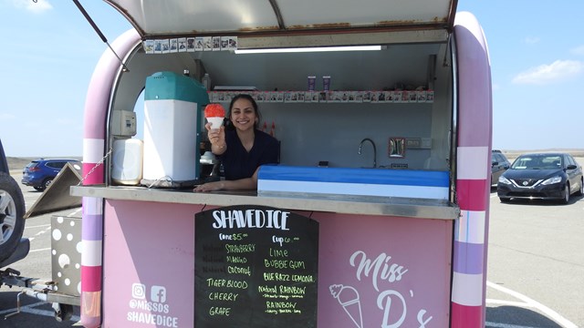 A person sells snow cones in a pink food truck.