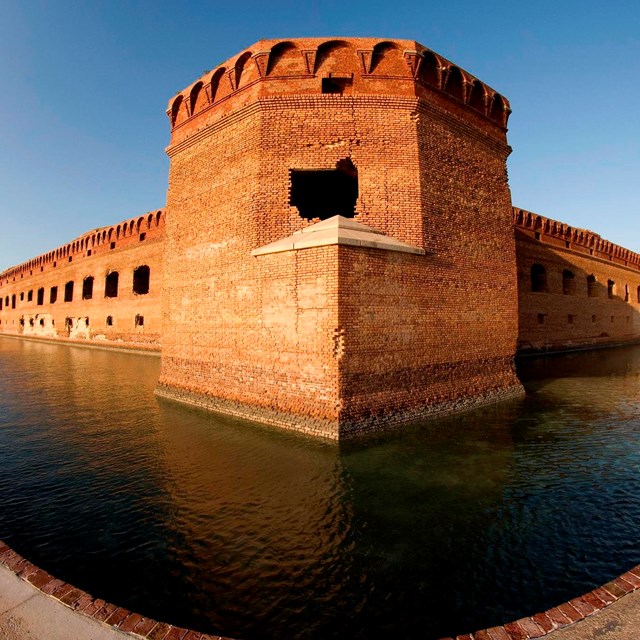 Large historic stone fort in a moat surrounded by and exterior wall and ocean