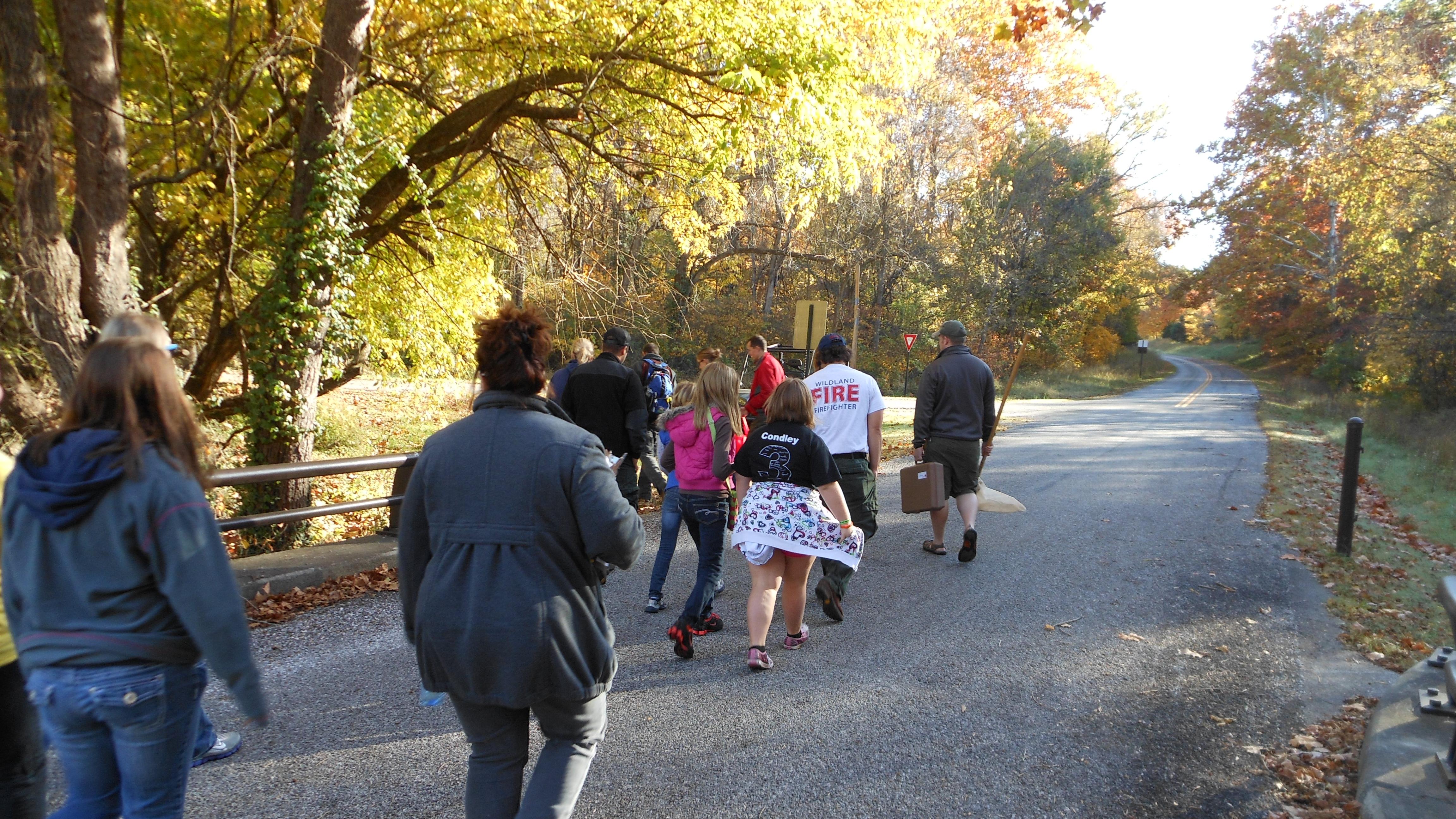 Photo of a group of people walking on a paved road with trees in the background
