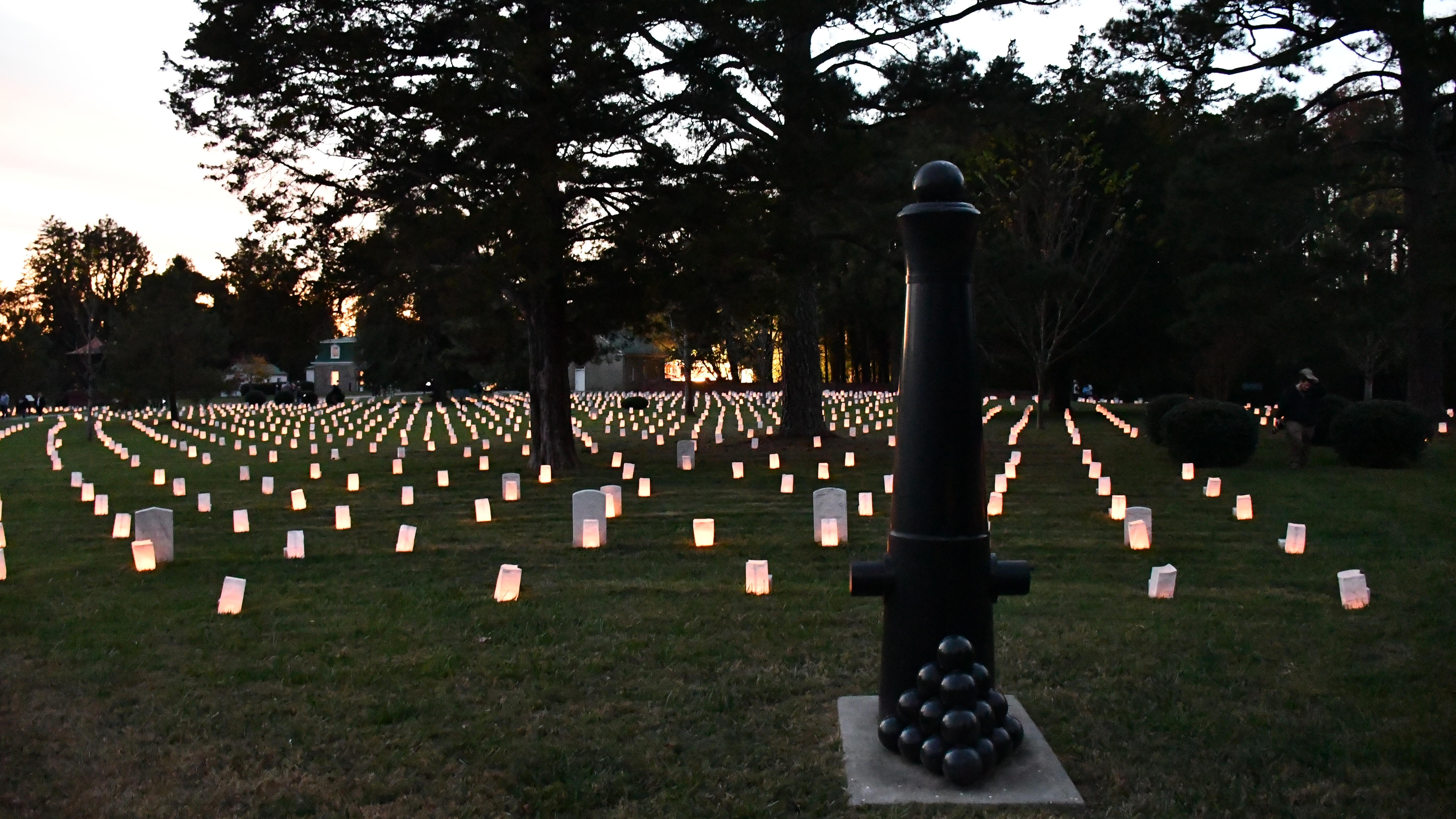 A pyramid of cannon balls in front of cannon tube in its end with luminaries in background.