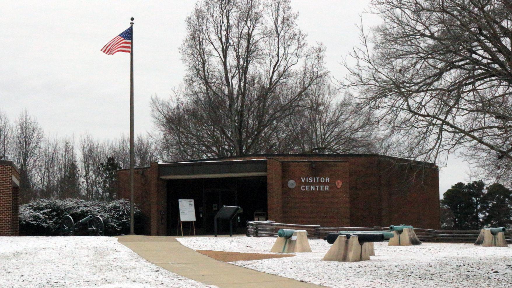 A U.S. flag flies in front of a brown brick building surrounded by snow on a cloudy day.