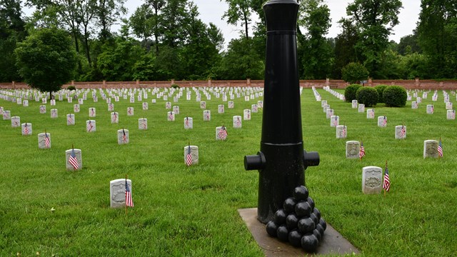 An inverted cannon tube in front of white headstones with flags.