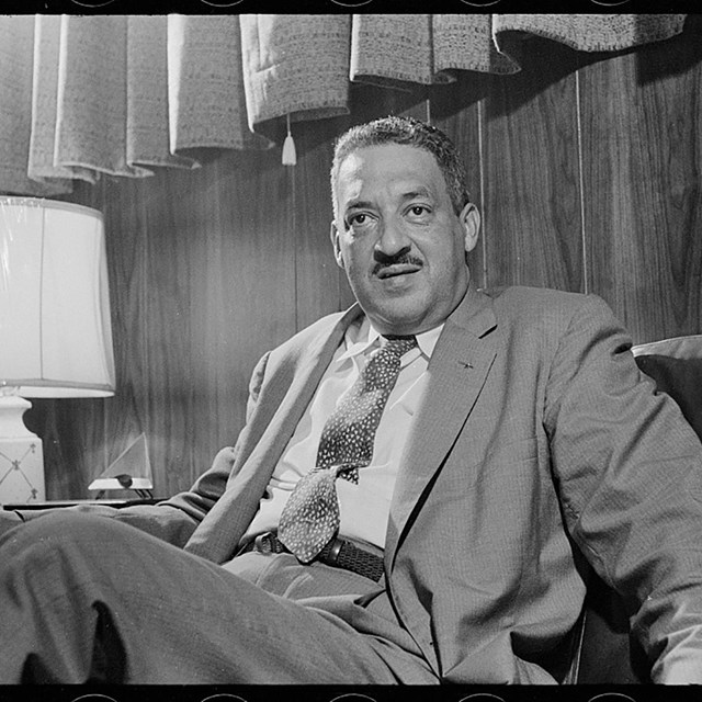 An older African American male with a mustache, wearing a suit and tie, seated in an armchair.