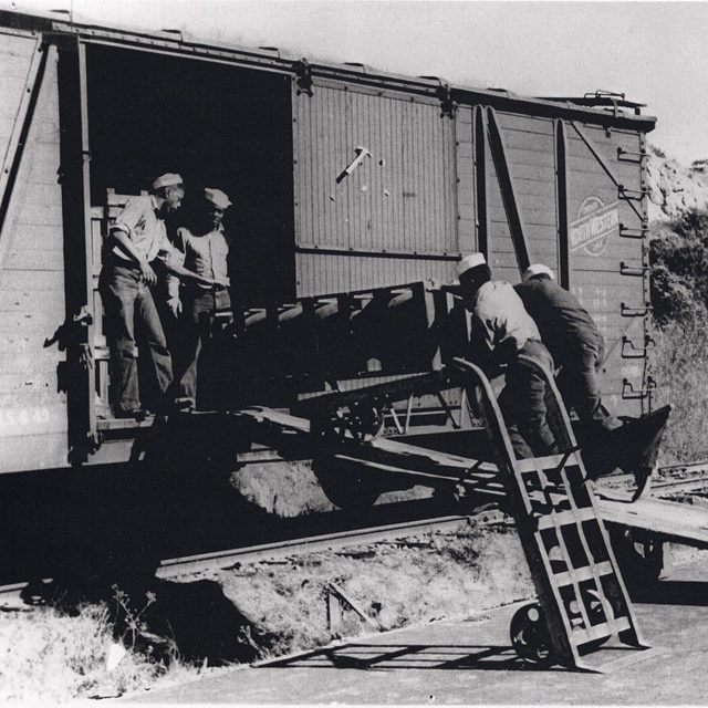 Historic photograph showing four African American sailors loading munitions into a boxcar.