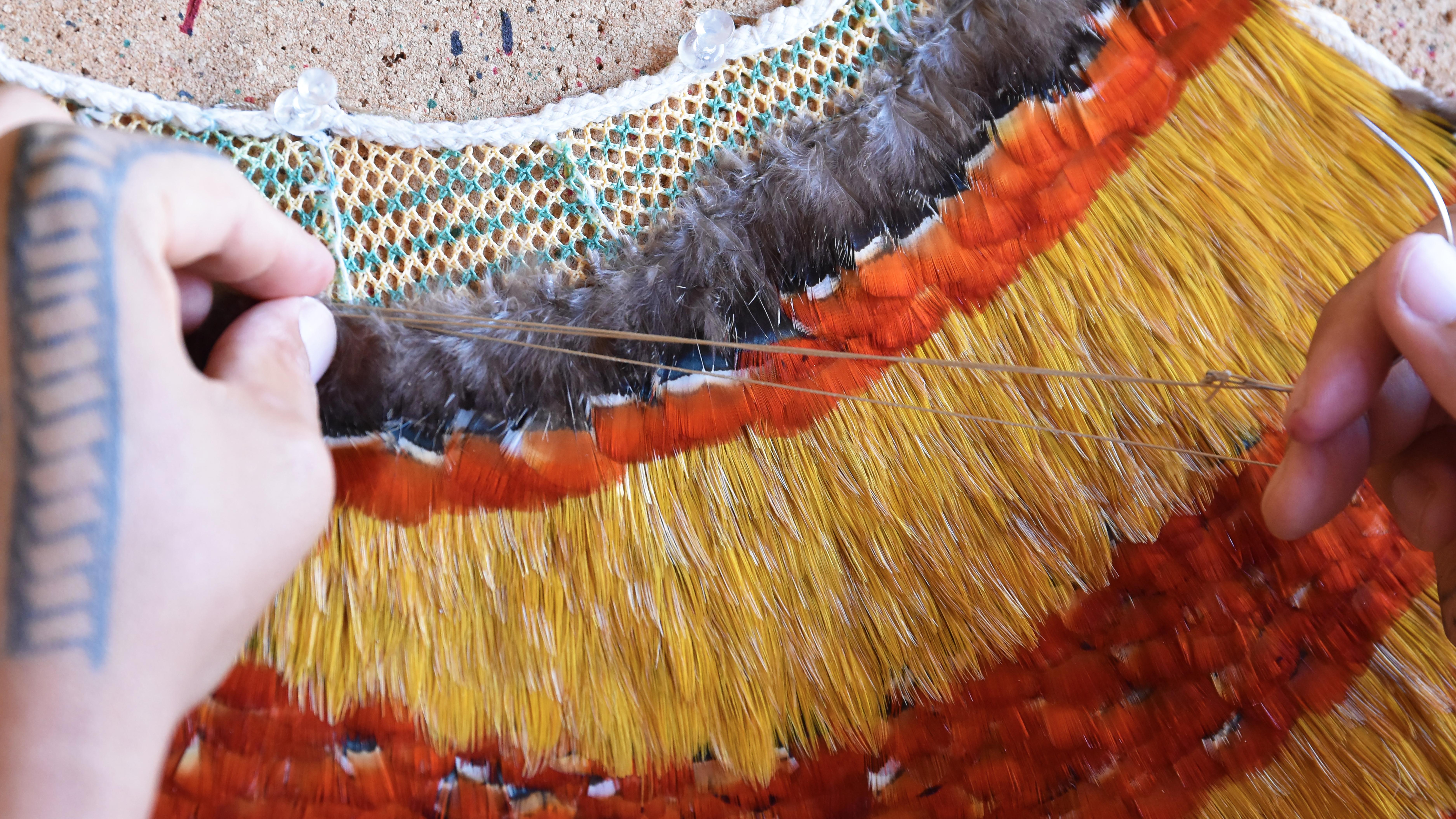 Close-up photograph of hand doing featherwork on a traditional Hawaiian cape
