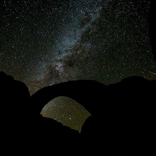 Silhouette of a sandstone arch with the Milky Way and many stars behind it