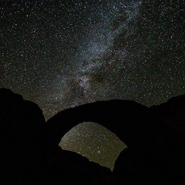 the milky way with silhouette of rainbow bridge in the foreground