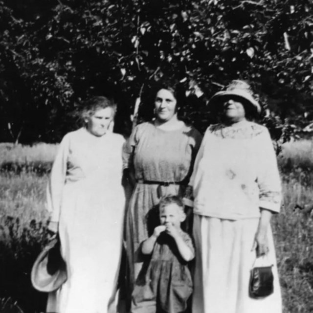 Black and white photo of three woman and a young boy in front of a tree