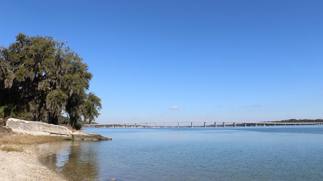 A fort on the edge of the water with a bridge in the background.