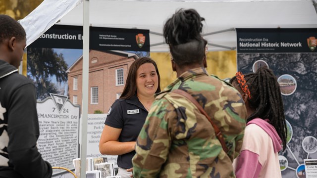 A woman in a Community Ambassador Volunteer uniform talking to visitors.