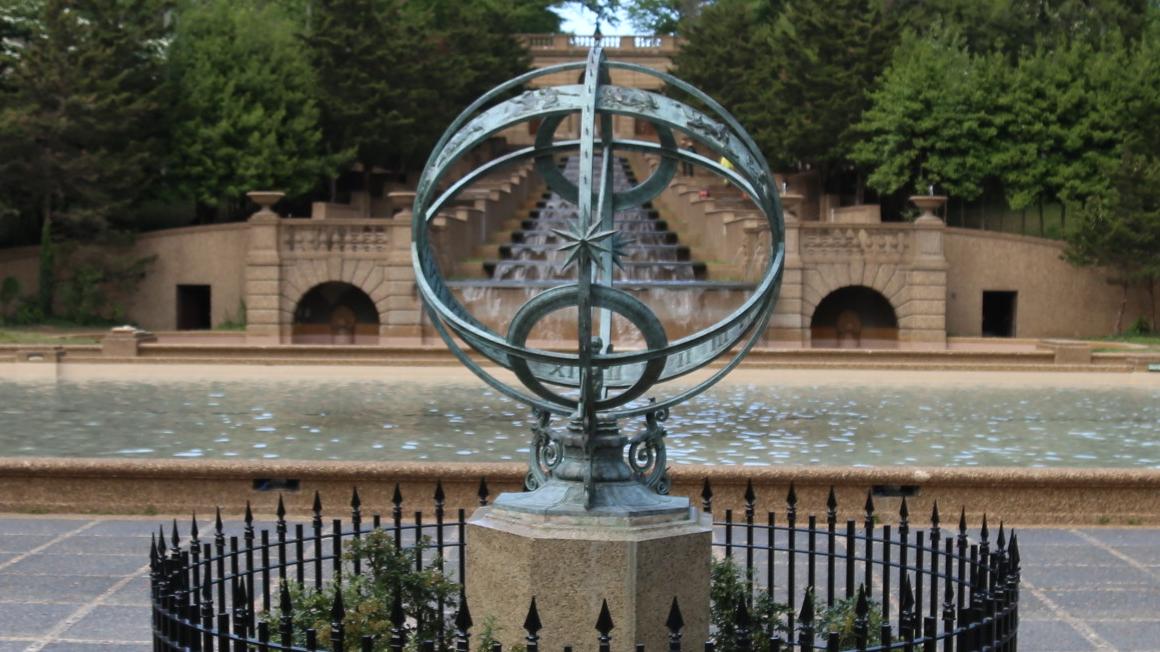 A green-tinted armillary sphere on a stone platform with a fence around it