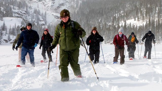 A group is participating on a ranger-led snowshoe hike