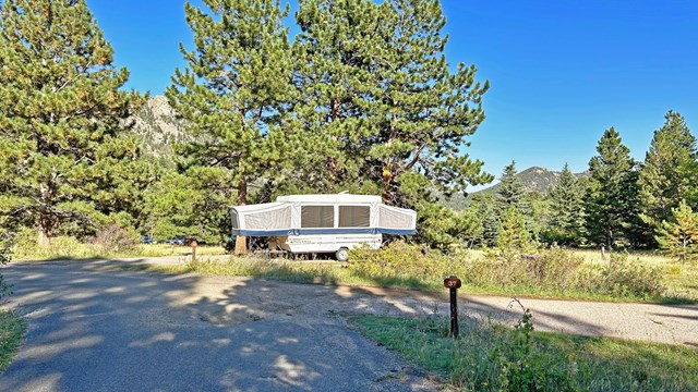 A pop up trailer is set up in a campsite in Aspenglen Campground