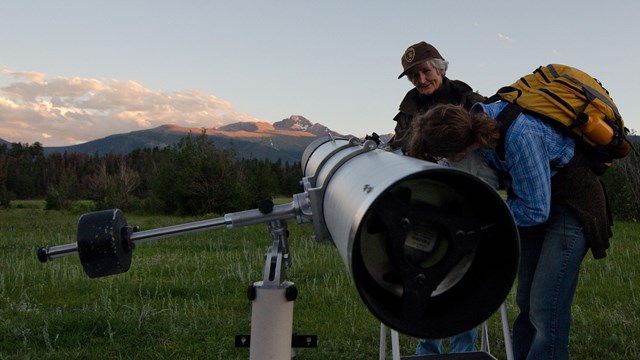 A park visitor is looking into a telescope to see the night sky.
