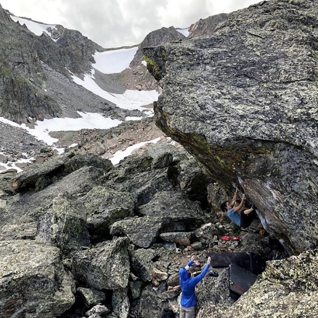 One person is climbing on a boulder problem while another person spots them.