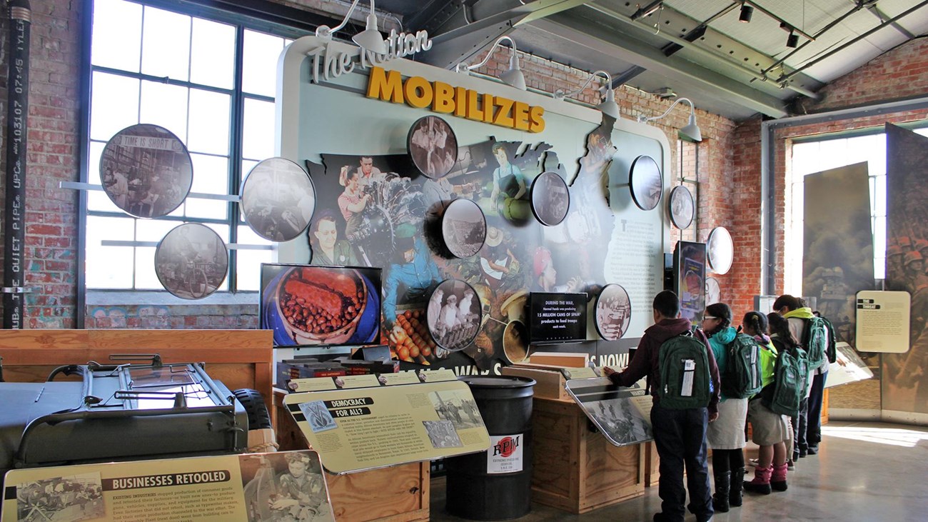 Children observe an interactive WWII exhibit with visuals and text explaining how the nation mobiliz