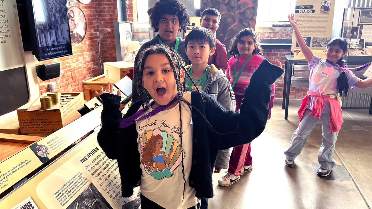 A group of children happily smile and pose in front of the visitor center exhibit.