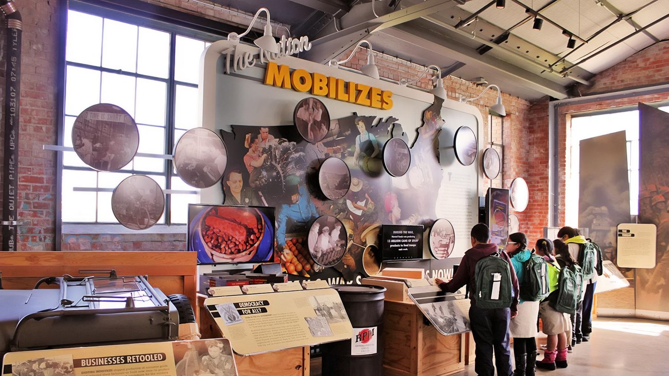 Children observe an interactive WWII exhibit with visuals and text explaining how the nation mobiliz