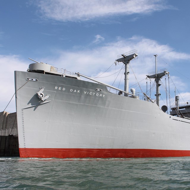 Photo of the SS Red Oak Victory Ship from the side as it's docked in the bay.