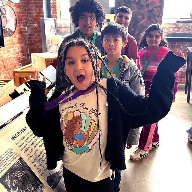 A group of children happily smile and pose in front of the visitor center exhibit.