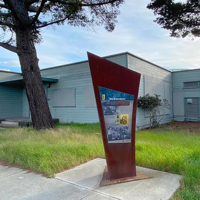 A single story building showing wear and tear. An interpretive sign and trees.