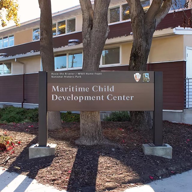 A wooden identification sign in front of a two story historic building. 