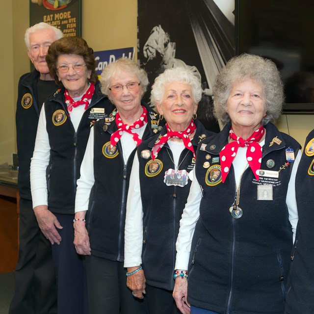 A group of four senior women and one senior male in volunteer uniforms pose for the camera. 