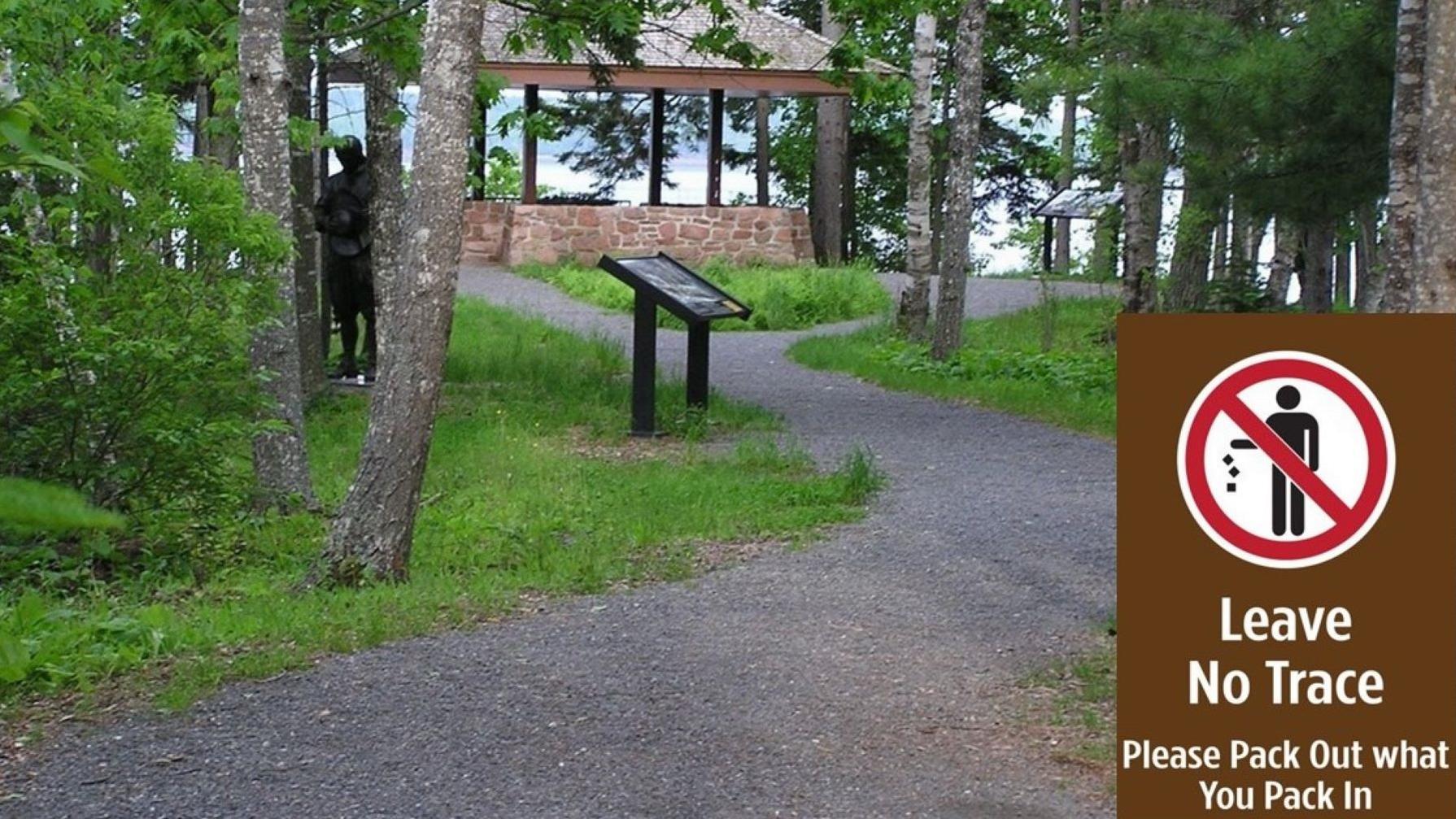 A path through the woods with statues and a small inset figure of human shape in the bottom right