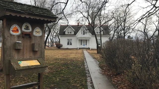 An erected wooden sign stands at the entry to a walkway to a historic home.