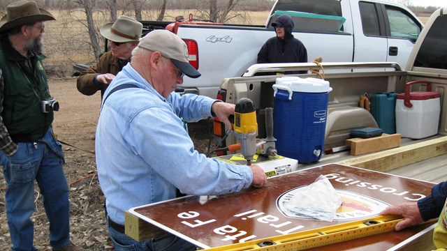 People work on a large metal sign in the back of a pickup truck.