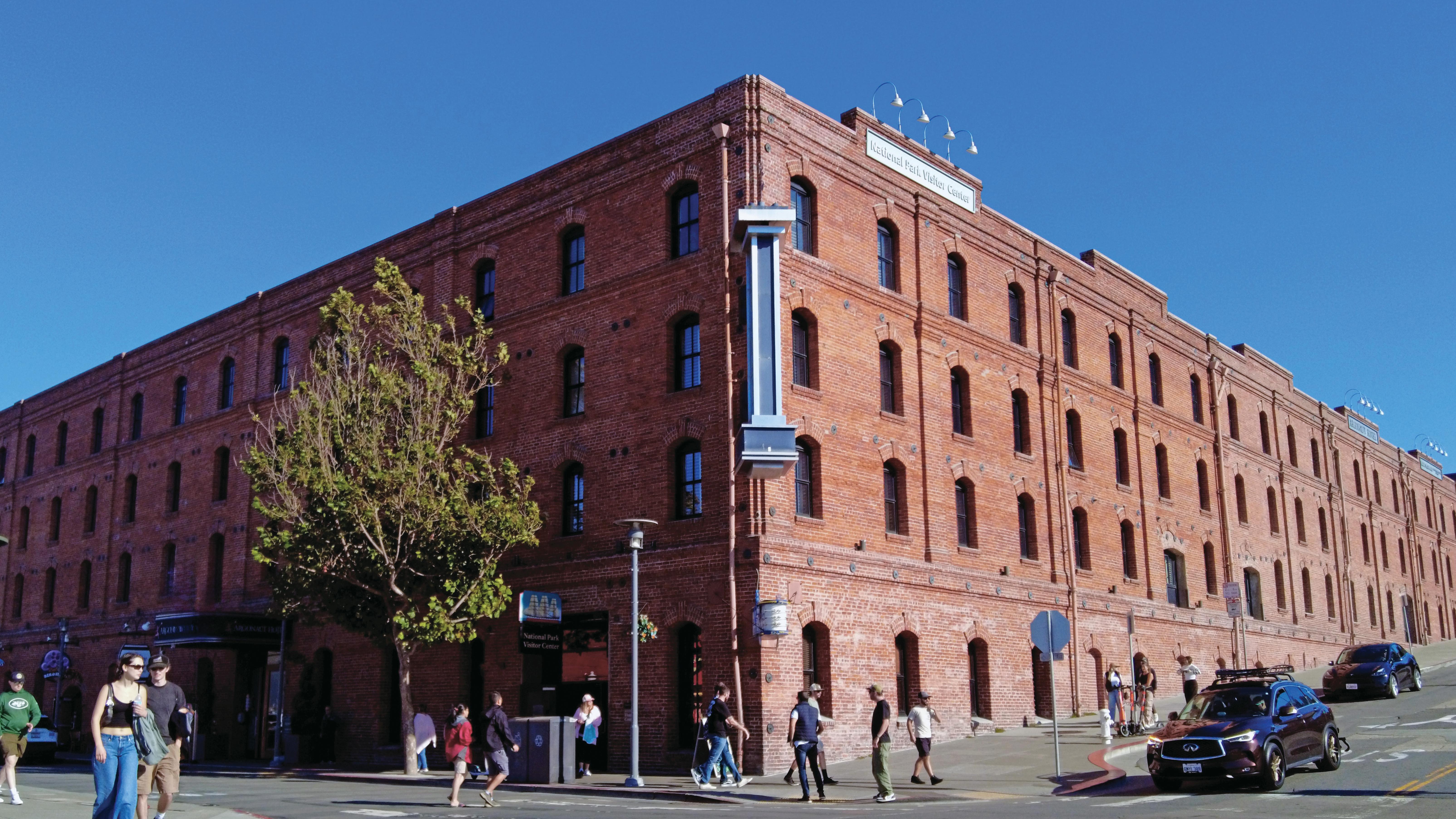 A historical brick warehouse stands on the corner of a busy street on a sunny day.