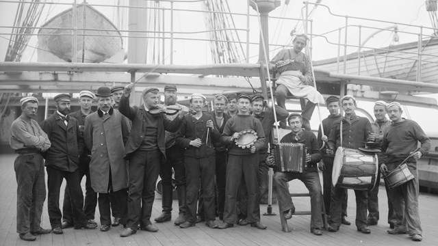 black and white image of men holding instruments standing on the deck of a ship.