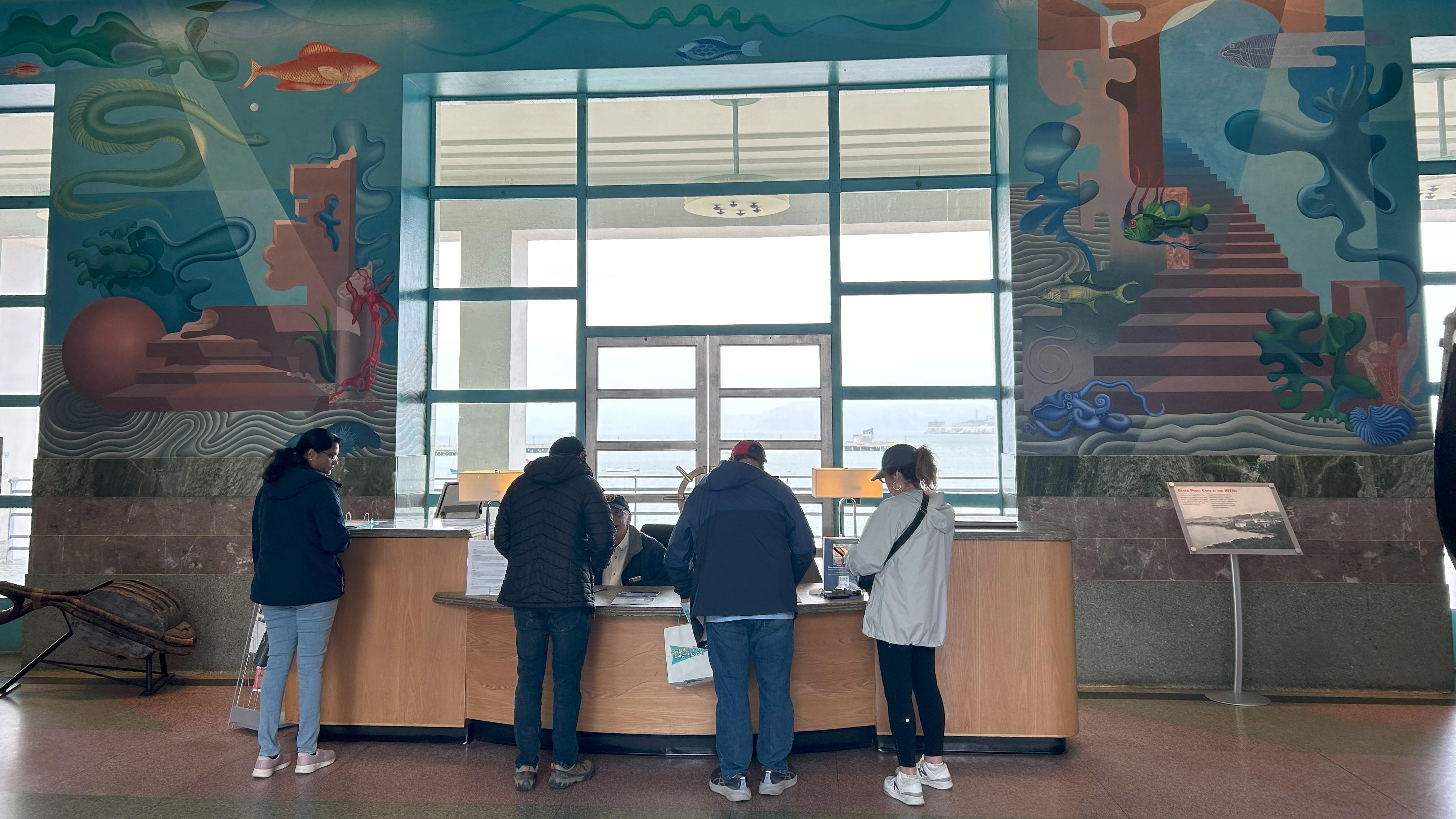 visitors stand at the information desk in the Maritime Museum, surrounded by murals.