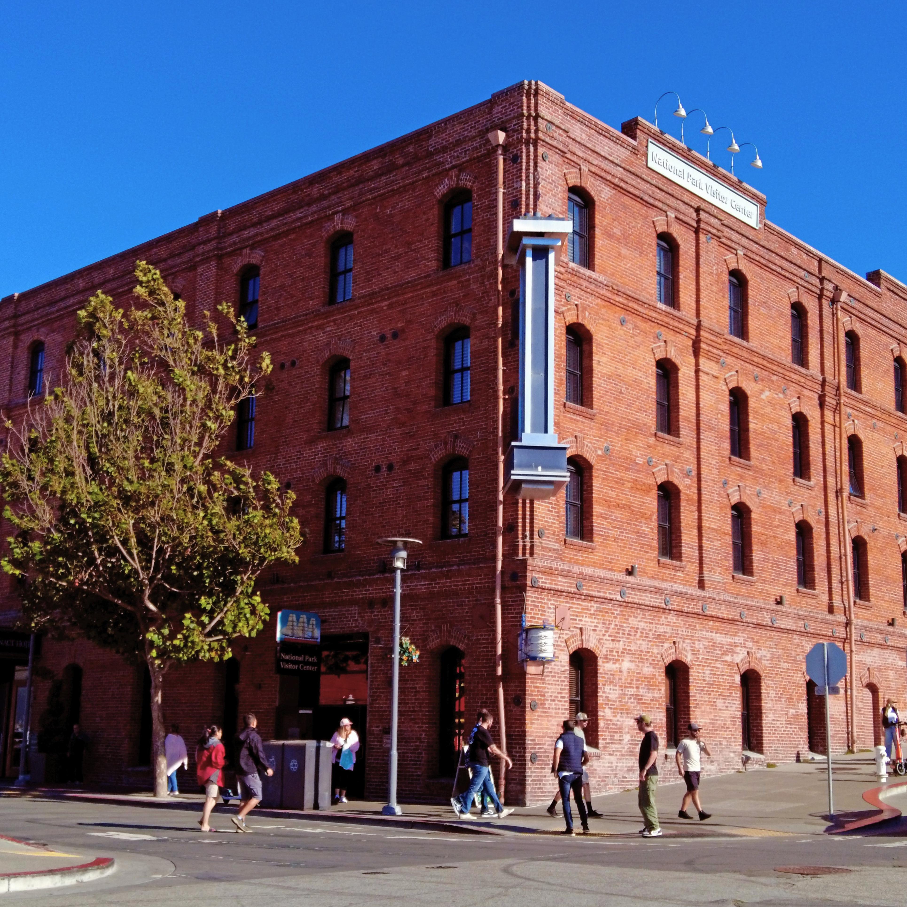 A historical brick warehouse stands on the corner of a busy street on a sunny day.