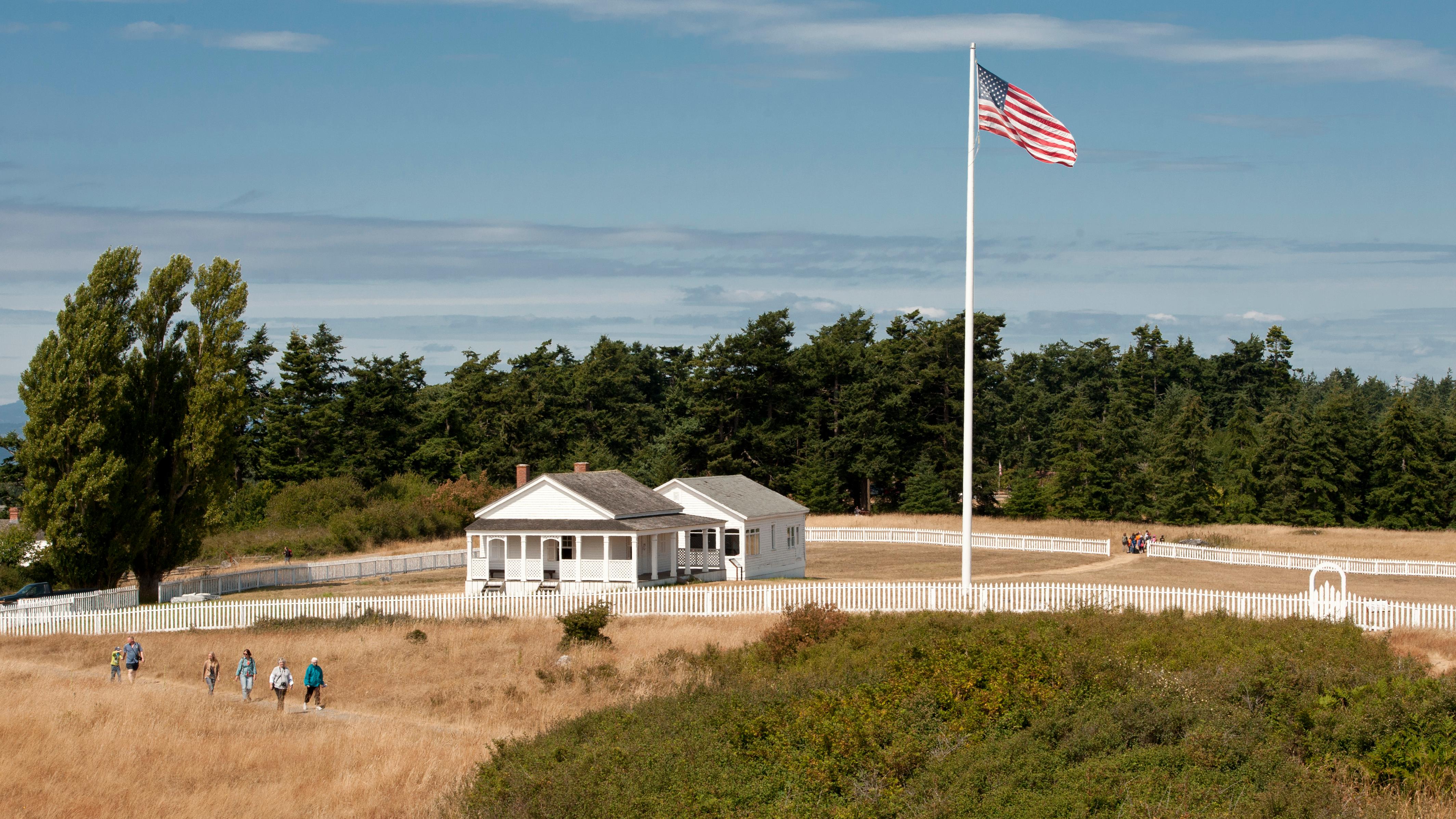 Historic white buildings in a fenced area with an American flag.