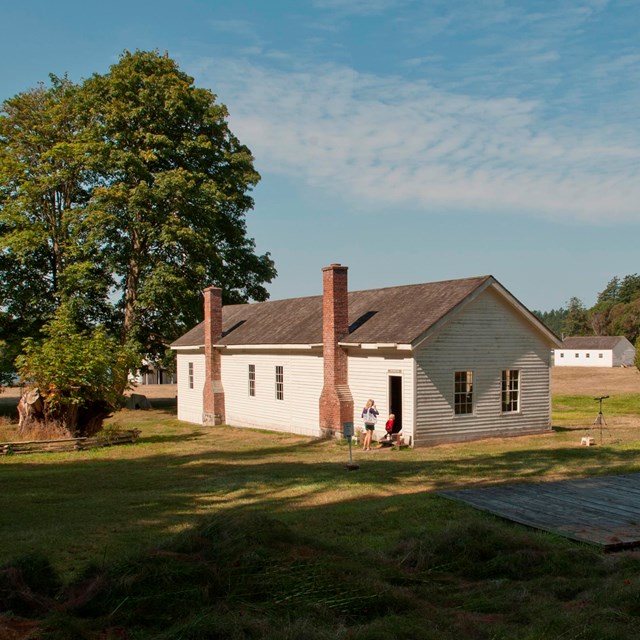 Historic white buildings in a grassy field with large trees