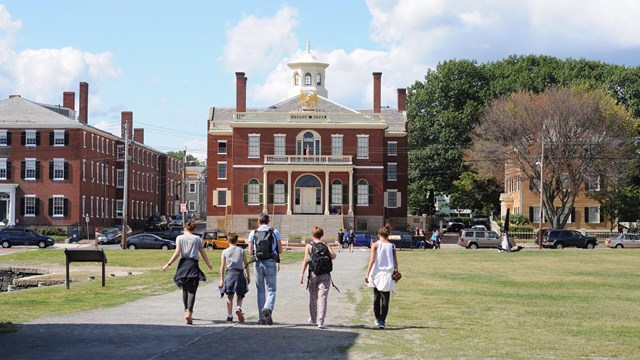 A group of five people walk toward a brick building.