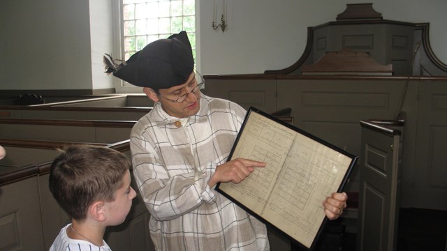 Young boy looking at document held by man dressed in colonial clothing