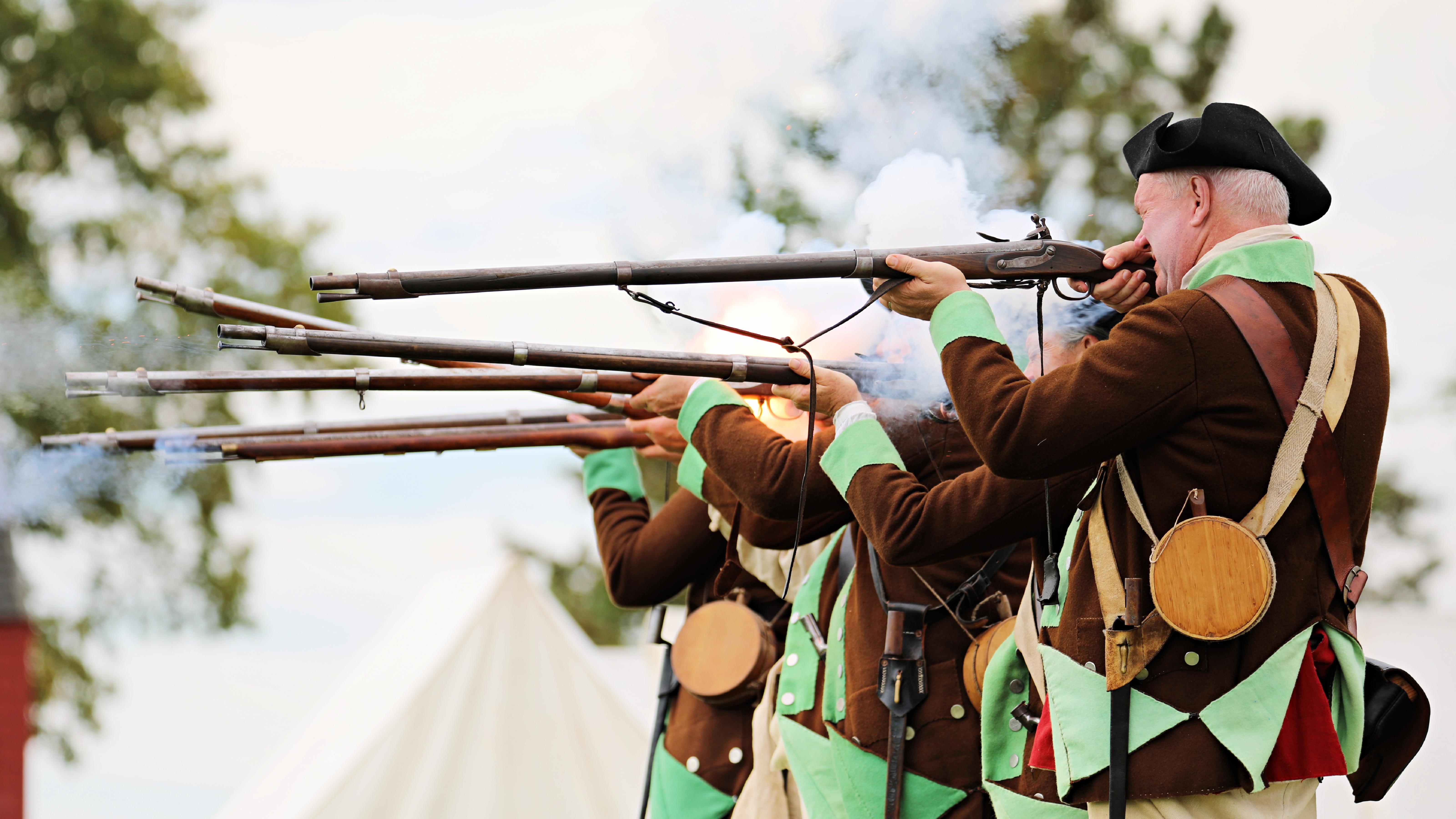 18th Century Soldiers in brown and green uniforms fire muskets.