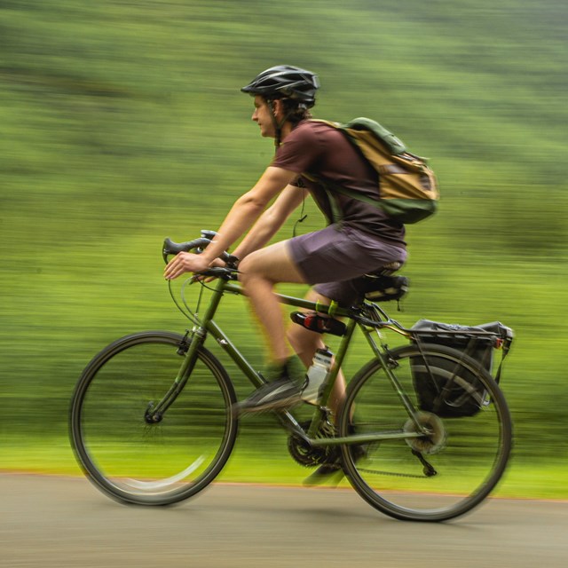 a man, wearing a helmet, bicycles on a path