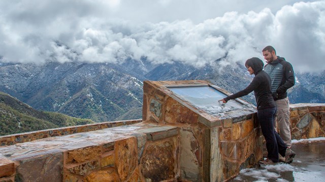 People read an exhibit at a snowy viewpoint. Photo by Kirke Wrench.