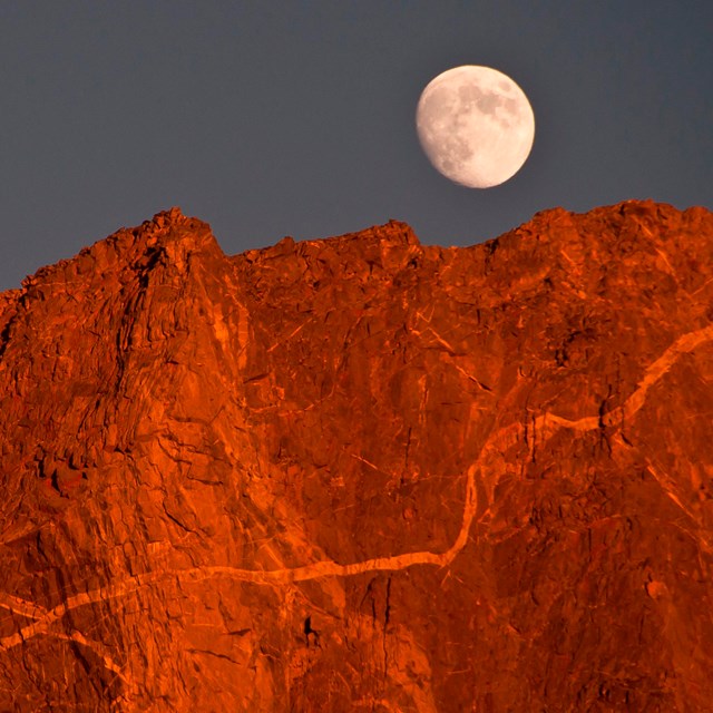 A moonrise over reddish peaks